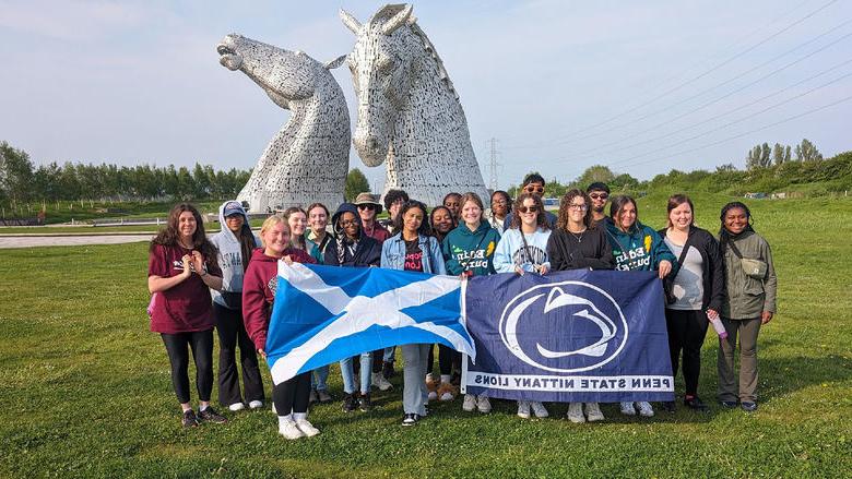 Students with a flag in front of twin horse statues